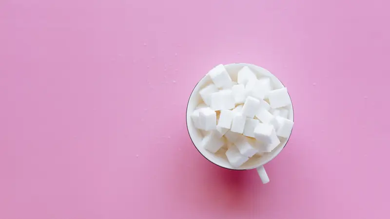 Tasse blanche remplie de morceaux de sucre sur un fond rose