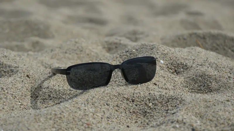 Lunettes de soleil à verres gris foncé posées sur le sable d'une plage