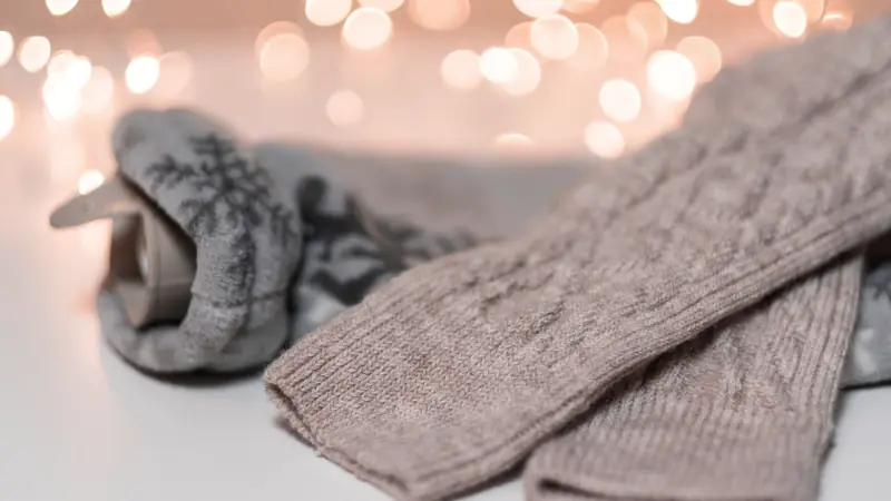 Bouillotte dans une housse tricotée posée près de chaussettes en laine