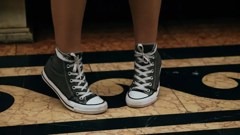 Jambes d'une personne debout en baskets montantes en toile sur un sol en marbre
