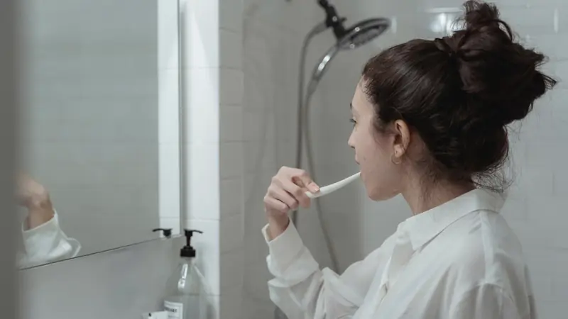 Personne qui se brosse les dents devant un miroir