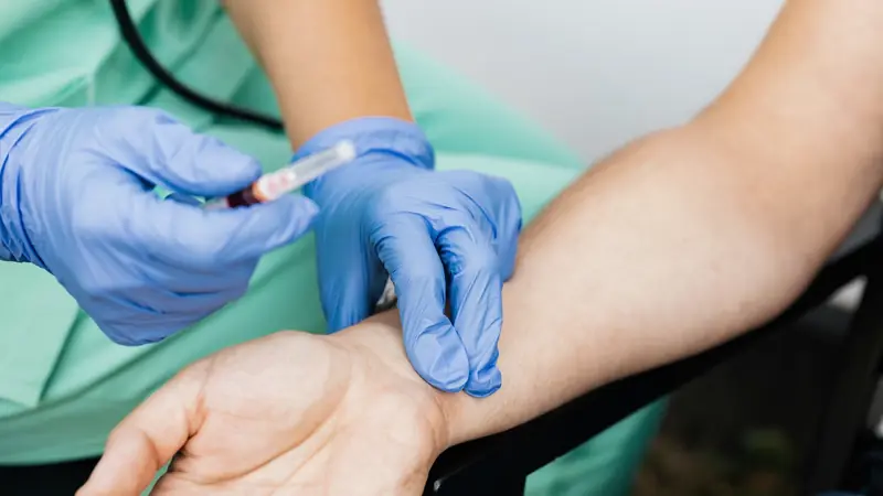 Mains gantées d'une soignante tenant un tube de sang près de l'avant-bras d'un patient