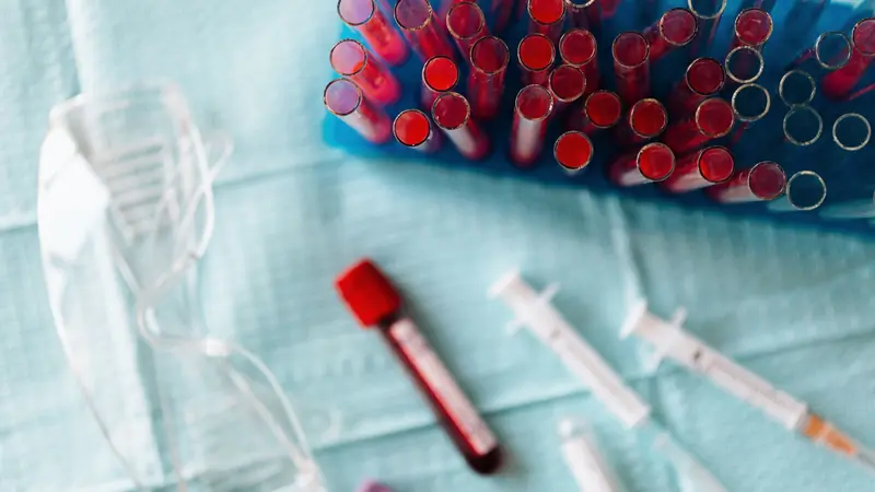 Tubes de sang dans un portoir bleu, tube de prélèvement, seringues et lunettes de protection sur un champ de soin