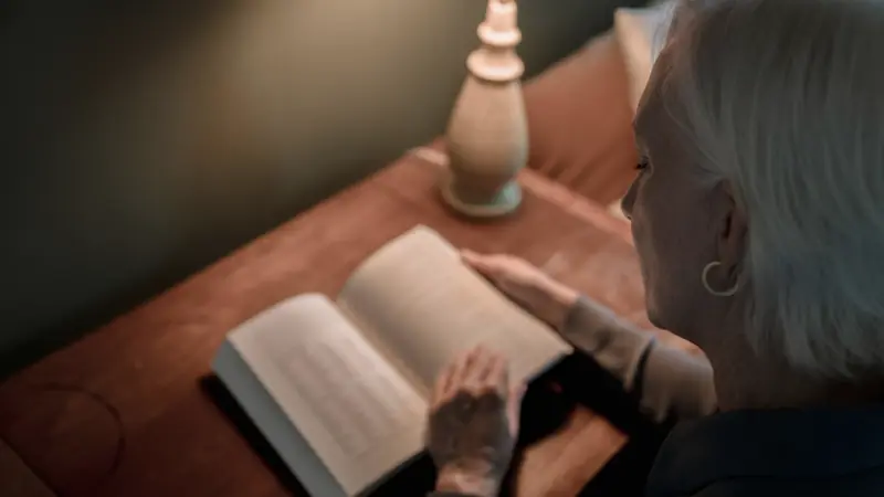 Femme qui lit un livre papier sous une lampe douce le soir