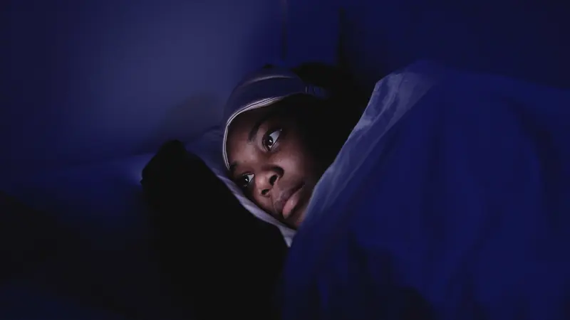 Personne allongée dans un lit, éveillée dans la pénombre