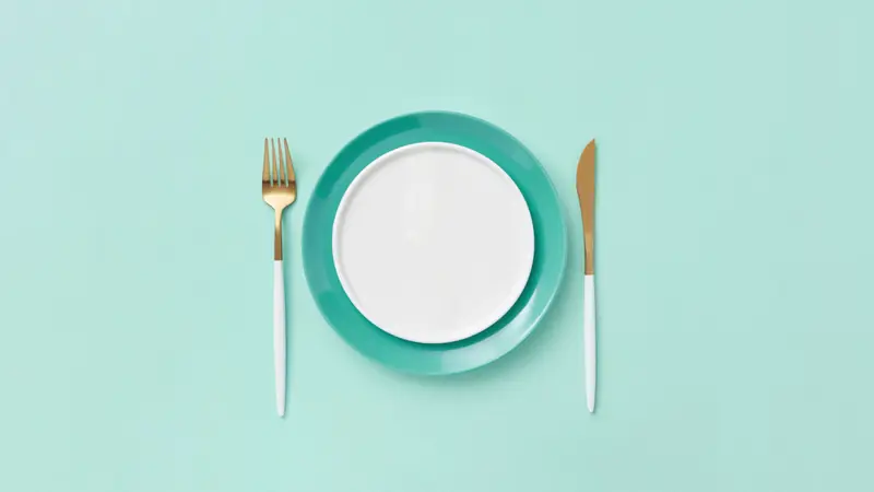Assiette vide et couverts sur un fond turquoise