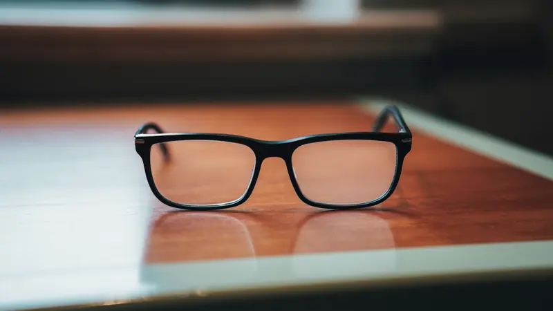 Lunettes de vue rectangulaires à monture noire posées sur une table en bois verni