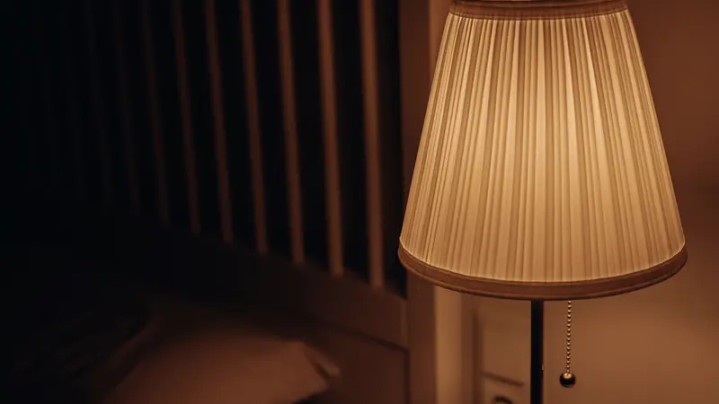 Lampe de chevet à abat-jour plissé diffusant une lumière chaude près d'un lit