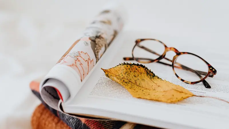 Lunettes à monture écaille posées sur un magazine ouvert avec une feuille d'automne