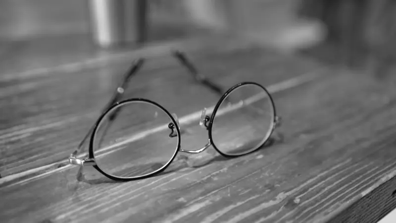 Lunettes rondes à fine monture métallique posées sur une table en bois, en noir et blanc