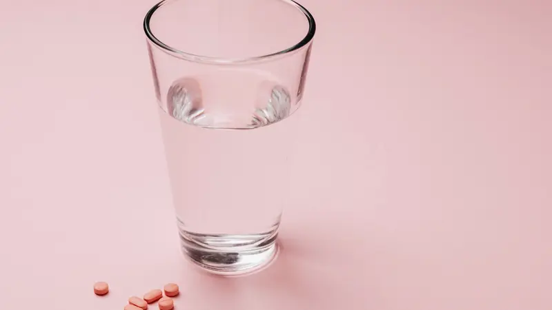 Verre d'eau et comprimés posés sur un fond rose