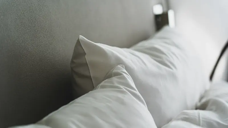 Gros plan sur des oreillers blancs et une couette contre une tête de lit grise