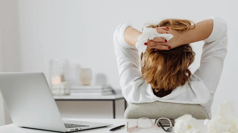 Femme vue de dos assise devant un ordinateur portable, les mains croisées derrière la tête