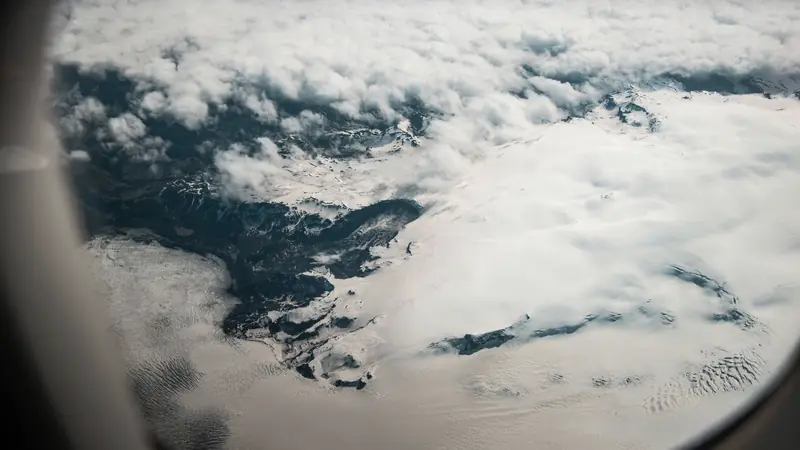 Vue par le hublot d'un avion sur des nuages et des montagnes enneigées