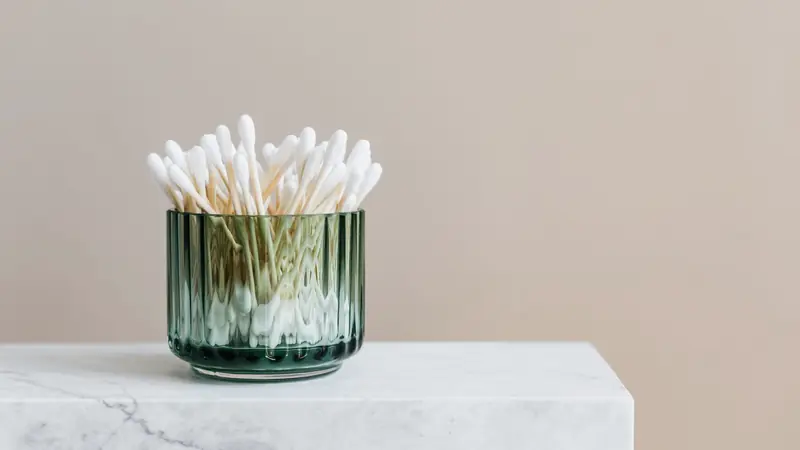 Cotons-tiges à bout blanc rangés dans un pot en verre vert posé sur un bloc de marbre