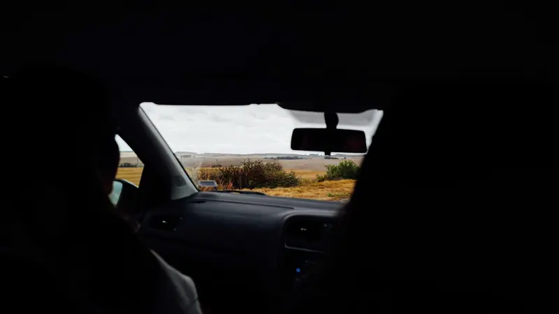 Vue depuis la banquette arrière d'une voiture sur une route de campagne, passagers en silhouette