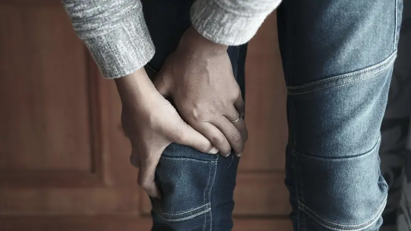 Personne en jean qui se tient la jambe à deux mains au niveau du genou