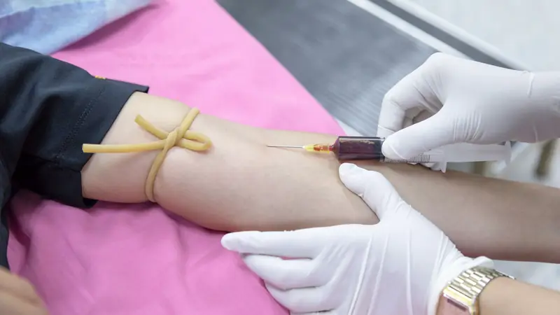 Infirmière qui pose un garrot avant une prise de sang au pli du coude