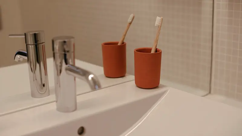 Lavabo blanc avec robinet chromé et deux gobelets en terre cuite contenant des brosses à dents en bambou