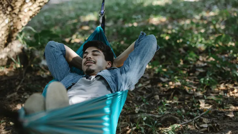 Personne qui se repose les yeux fermés dans un hamac à l'ombre