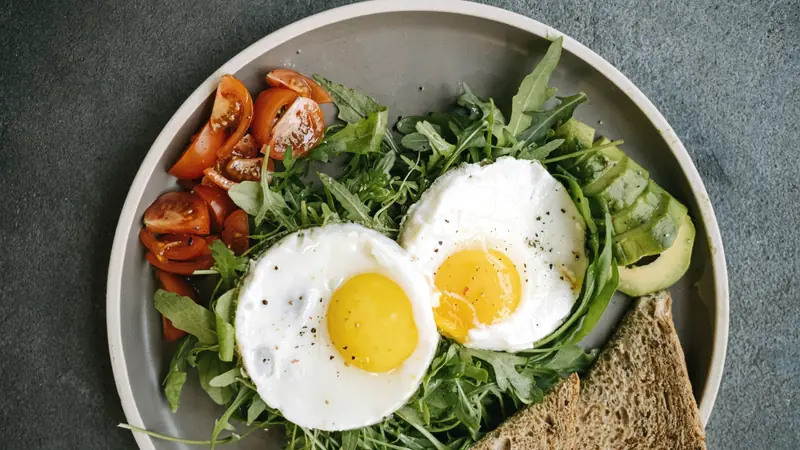Assiette de petit-déjeuner avec deux œufs au plat sur de la roquette, des tomates cerises, de l'avocat et du pain complet grillé