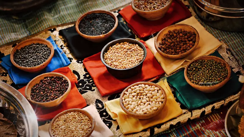 Bols en terre cuite remplis de légumineuses et de céréales (pois chiches, haricots blancs, haricots mungo, blé) posés sur des tissus colorés